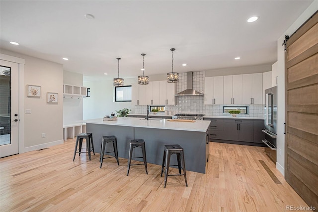 kitchen with a kitchen island with sink, light hardwood / wood-style floors, wall chimney range hood, and white cabinetry