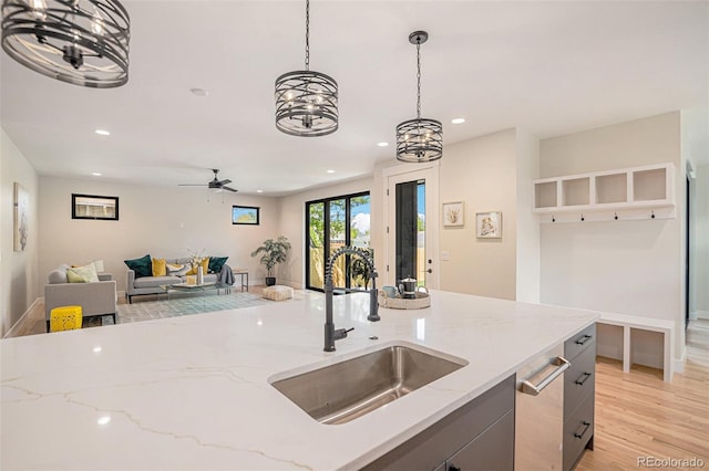 kitchen featuring pendant lighting, light stone countertops, light wood-type flooring, sink, and ceiling fan