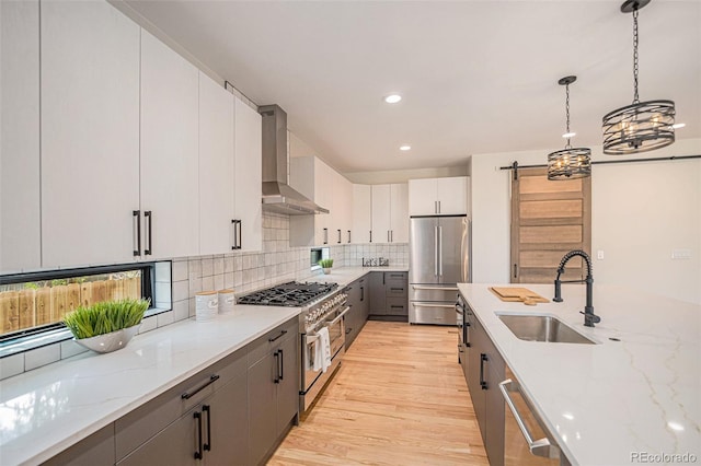 kitchen featuring decorative light fixtures, wall chimney range hood, stainless steel appliances, sink, and light hardwood / wood-style floors