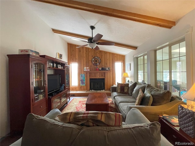 living room featuring vaulted ceiling with beams, a fireplace with flush hearth, a ceiling fan, wooden walls, and a textured ceiling