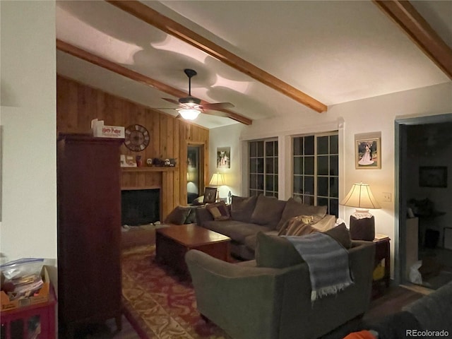 living area with vaulted ceiling with beams, wood walls, a fireplace, and a ceiling fan