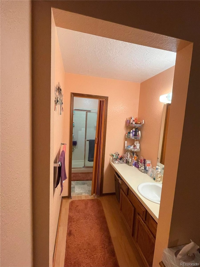 bathroom featuring double vanity, wood finished floors, an enclosed shower, a textured ceiling, and a sink