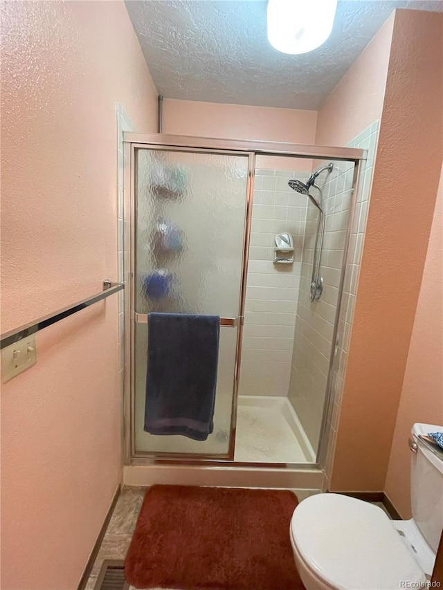 bathroom with a shower with shower door, a textured ceiling, and toilet