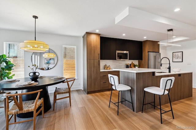 kitchen with light wood-type flooring, modern cabinets, stainless steel appliances, a breakfast bar area, and light countertops