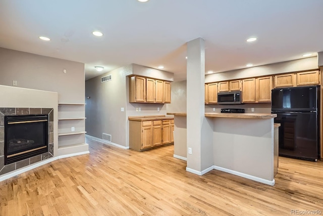 kitchen with black refrigerator, light wood-type flooring, and a tile fireplace