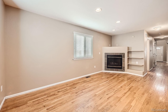 unfurnished living room featuring a tile fireplace and light wood-type flooring