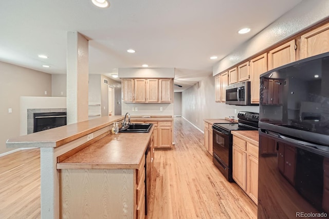 kitchen featuring light brown cabinetry, light wood-type flooring, sink, black appliances, and a fireplace