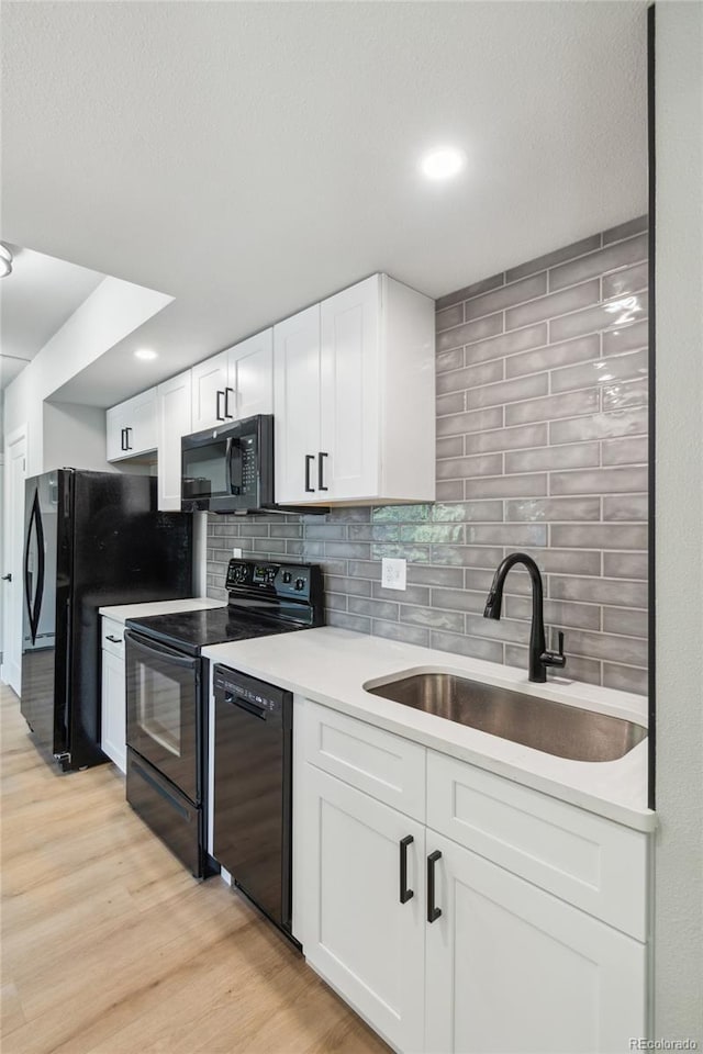 kitchen with backsplash, black appliances, sink, light hardwood / wood-style floors, and white cabinetry