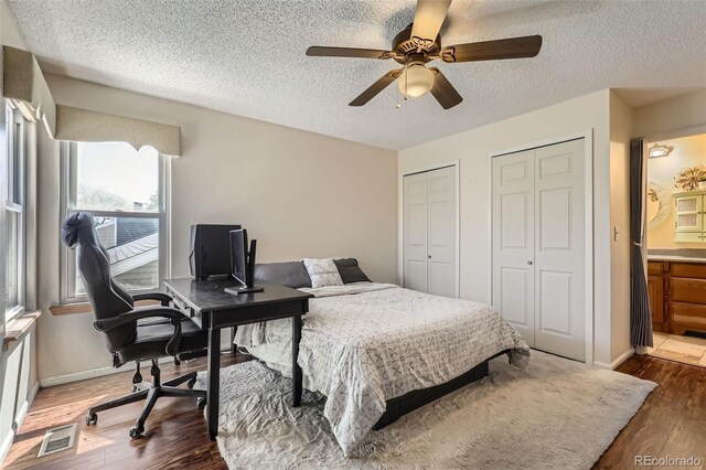 bedroom featuring ceiling fan, a textured ceiling, visible vents, wood finished floors, and two closets