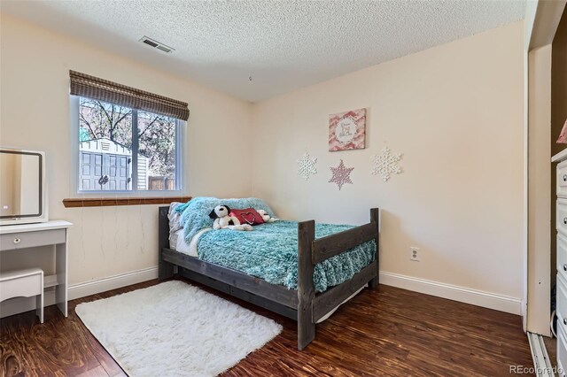 bedroom with baseboards, a textured ceiling, wood finished floors, and visible vents