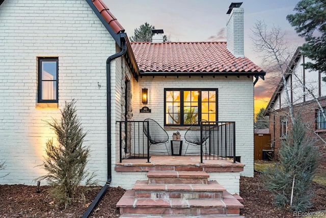 rear view of house with a tiled roof, brick siding, and a chimney