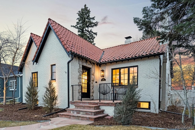 view of front of home with brick siding, a chimney, and a tiled roof