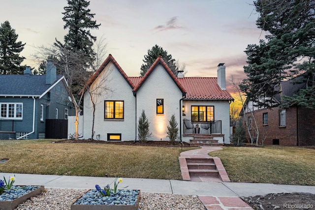 view of front of house with a tiled roof, a chimney, a front lawn, and brick siding