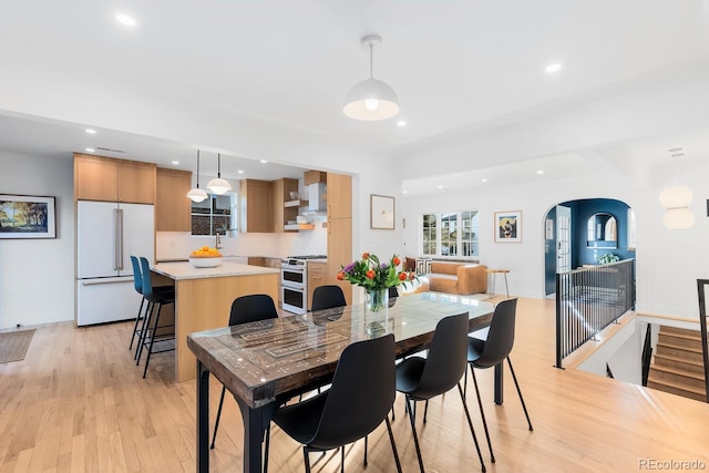 dining space featuring light wood finished floors, baseboards, arched walkways, and recessed lighting