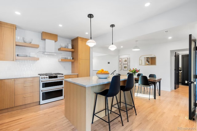 kitchen featuring a breakfast bar area, open shelves, light wood-type flooring, double oven range, and wall chimney exhaust hood