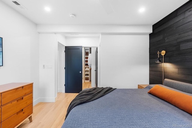 bedroom with light wood-style floors, visible vents, wooden walls, and baseboards