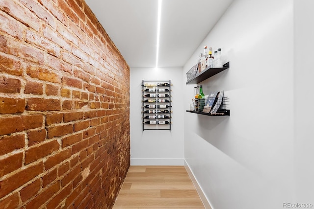 hall with light wood-style floors, baseboards, and brick wall