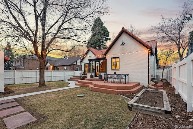 back of house with brick siding, a lawn, a fenced backyard, a garden, and a tiled roof