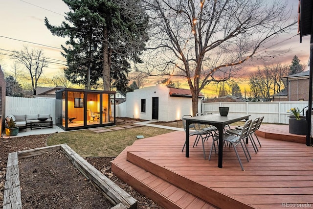 deck at dusk featuring a garden, an outbuilding, fence, outdoor dining area, and a yard