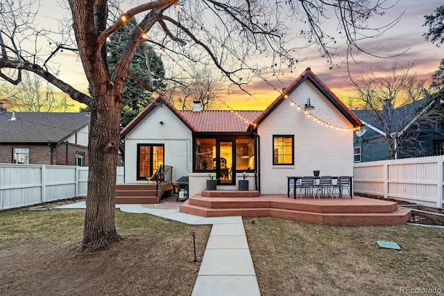 back of house at dusk with brick siding, fence, a lawn, and a patio