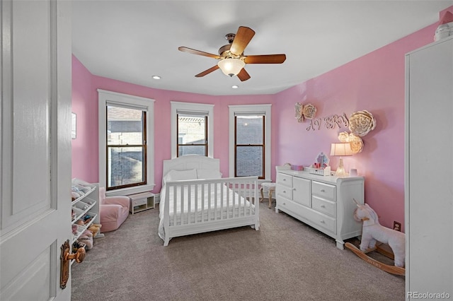 carpeted bedroom with ceiling fan and a crib