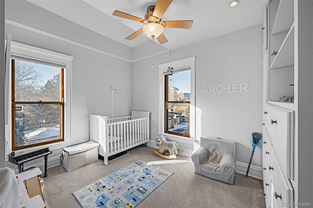 carpeted bedroom featuring ceiling fan and a crib