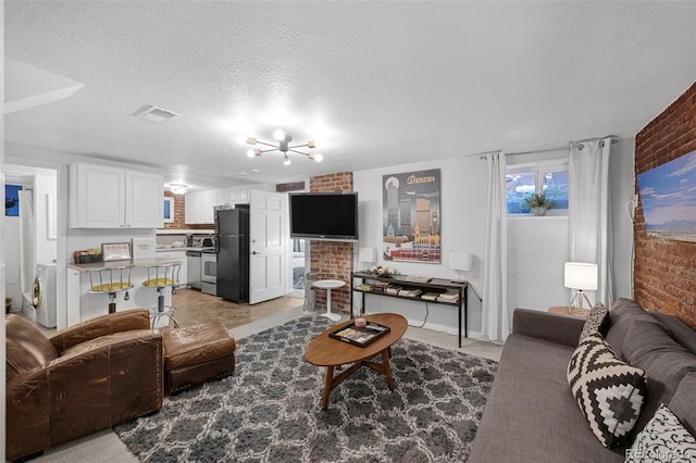 living room featuring washer / dryer, a textured ceiling, brick wall, and an inviting chandelier