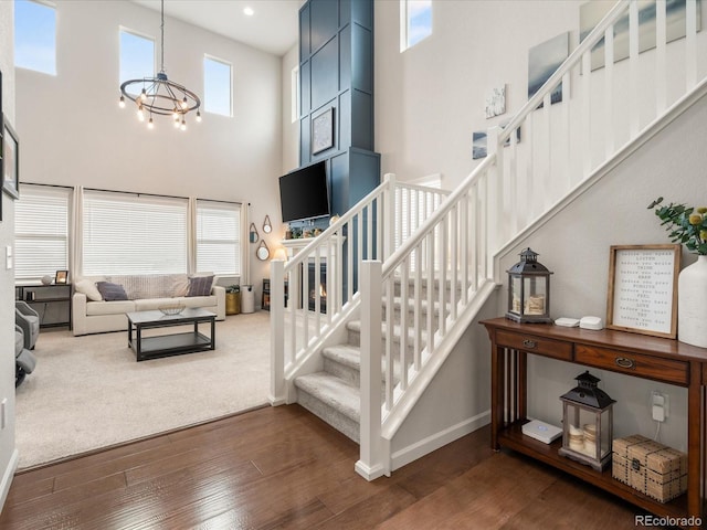 staircase with a chandelier, a towering ceiling, baseboards, and wood finished floors