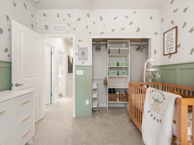 bedroom featuring light carpet, a wainscoted wall, visible vents, and wallpapered walls