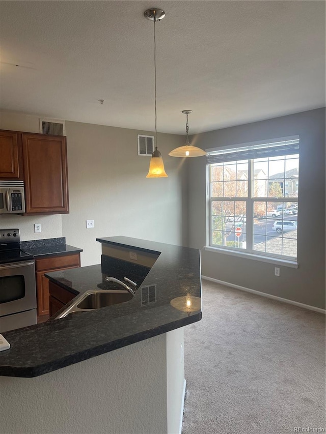 kitchen with light carpet, appliances with stainless steel finishes, decorative light fixtures, sink, and dark stone countertops