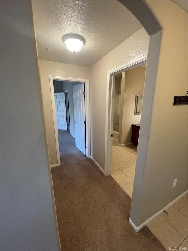 hallway with a textured ceiling and light carpet