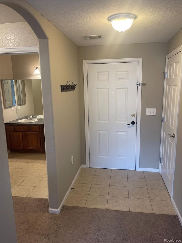 doorway featuring sink, light tile patterned floors, and a textured ceiling