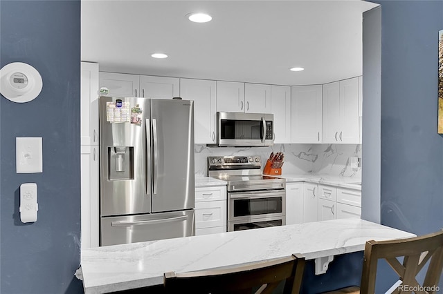 14300 E Marina Dr Unit 109, Aurora, CO 80014 - kitchen featuring appliances with stainless steel finishes, light stone countertops, white cabinets, recessed lighting, and a kitchen breakfast bar