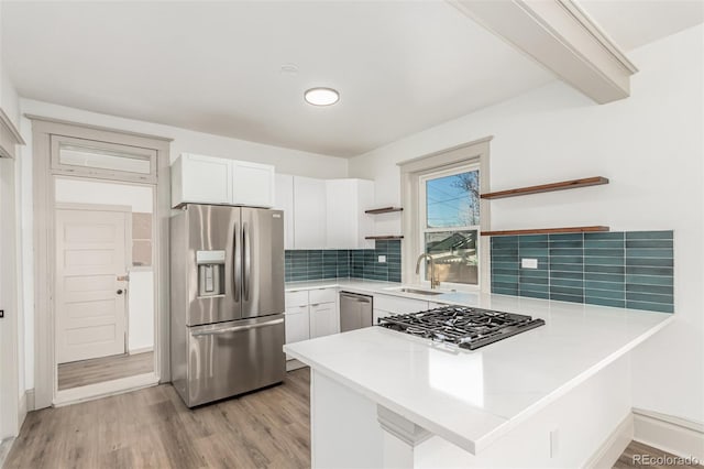 kitchen with stainless steel appliances, a peninsula, a sink, light wood-type flooring, and open shelves