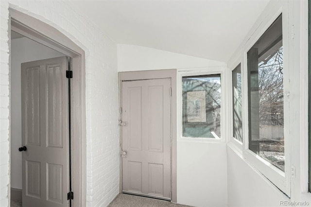 corridor featuring lofted ceiling, brick wall, and carpet floors