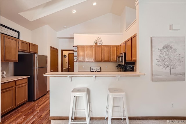 kitchen featuring stainless steel appliances, brown cabinets, a breakfast bar, high vaulted ceiling, and a peninsula