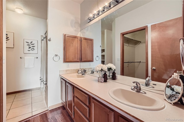 full bath featuring double vanity, a walk in closet, baseboards, and wood finished floors