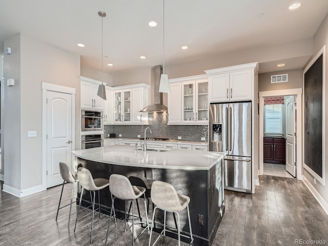 kitchen with visible vents, a sink, decorative backsplash, appliances with stainless steel finishes, and wall chimney exhaust hood