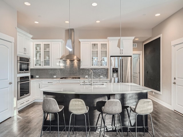 kitchen featuring backsplash, wall chimney range hood, an island with sink, appliances with stainless steel finishes, and a sink