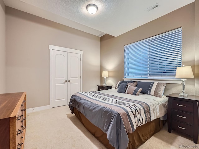 bedroom with visible vents, baseboards, light colored carpet, a closet, and a textured ceiling