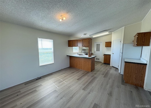 15125 Ewing Ct, Peyton, CO 80831 - kitchen with a peninsula, brown cabinets, a textured ceiling, light wood-style floors, and freestanding refrigerator