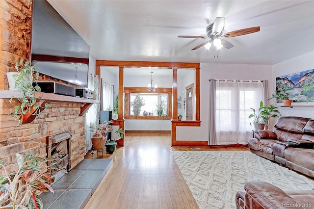 living room with ceiling fan with notable chandelier, a healthy amount of sunlight, hardwood / wood-style floors, and a fireplace