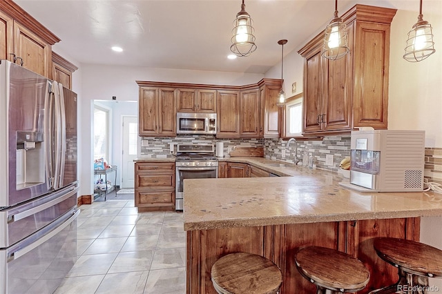 kitchen with a kitchen bar, sink, hanging light fixtures, kitchen peninsula, and stainless steel appliances