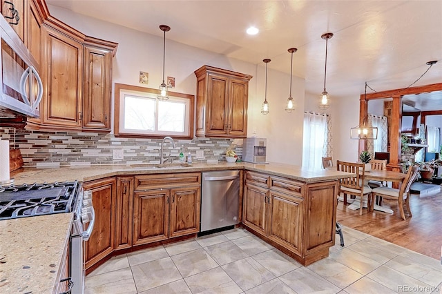 kitchen featuring appliances with stainless steel finishes, pendant lighting, sink, decorative backsplash, and kitchen peninsula