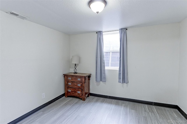 spare room featuring light hardwood / wood-style floors and a textured ceiling