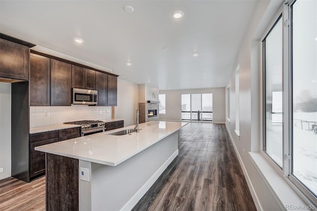 kitchen with dark brown cabinetry, sink, stainless steel appliances, hardwood / wood-style floors, and an island with sink