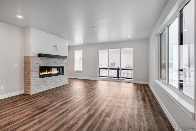 unfurnished living room with plenty of natural light, dark hardwood / wood-style floors, and a stone fireplace