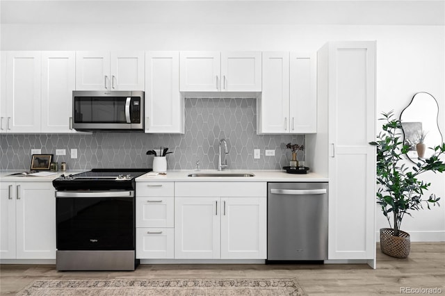 kitchen featuring light wood-style flooring, stainless steel appliances, a sink, light countertops, and tasteful backsplash