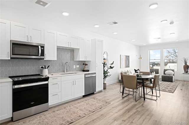 kitchen with visible vents, light wood-style flooring, appliances with stainless steel finishes, light countertops, and a sink