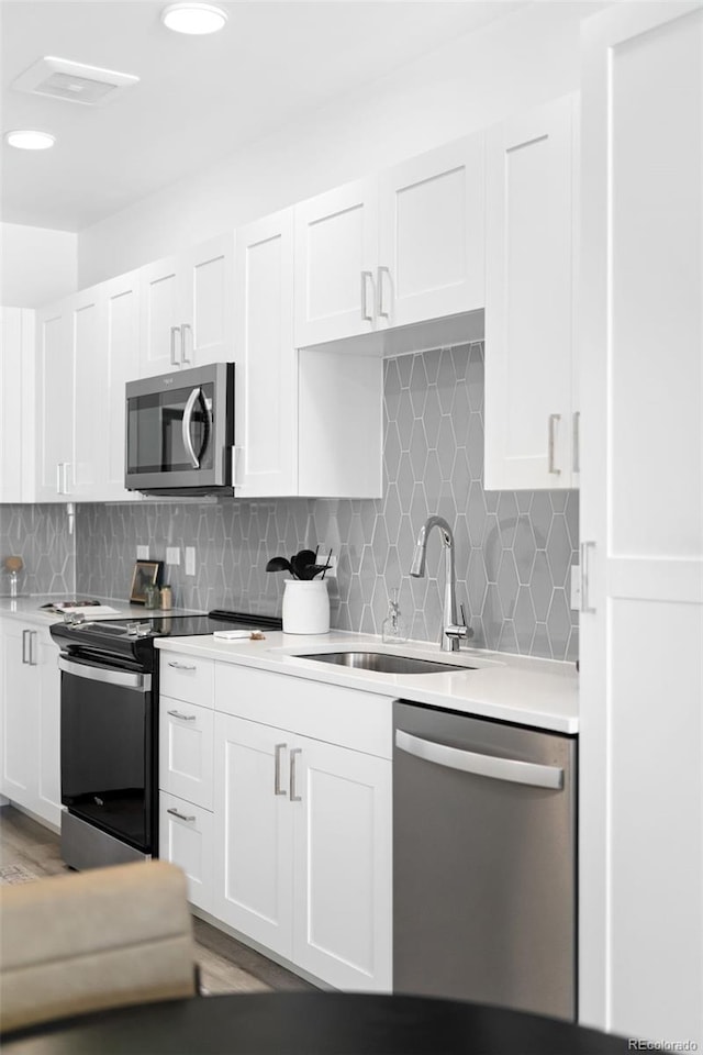 kitchen with tasteful backsplash, light countertops, appliances with stainless steel finishes, white cabinets, and a sink